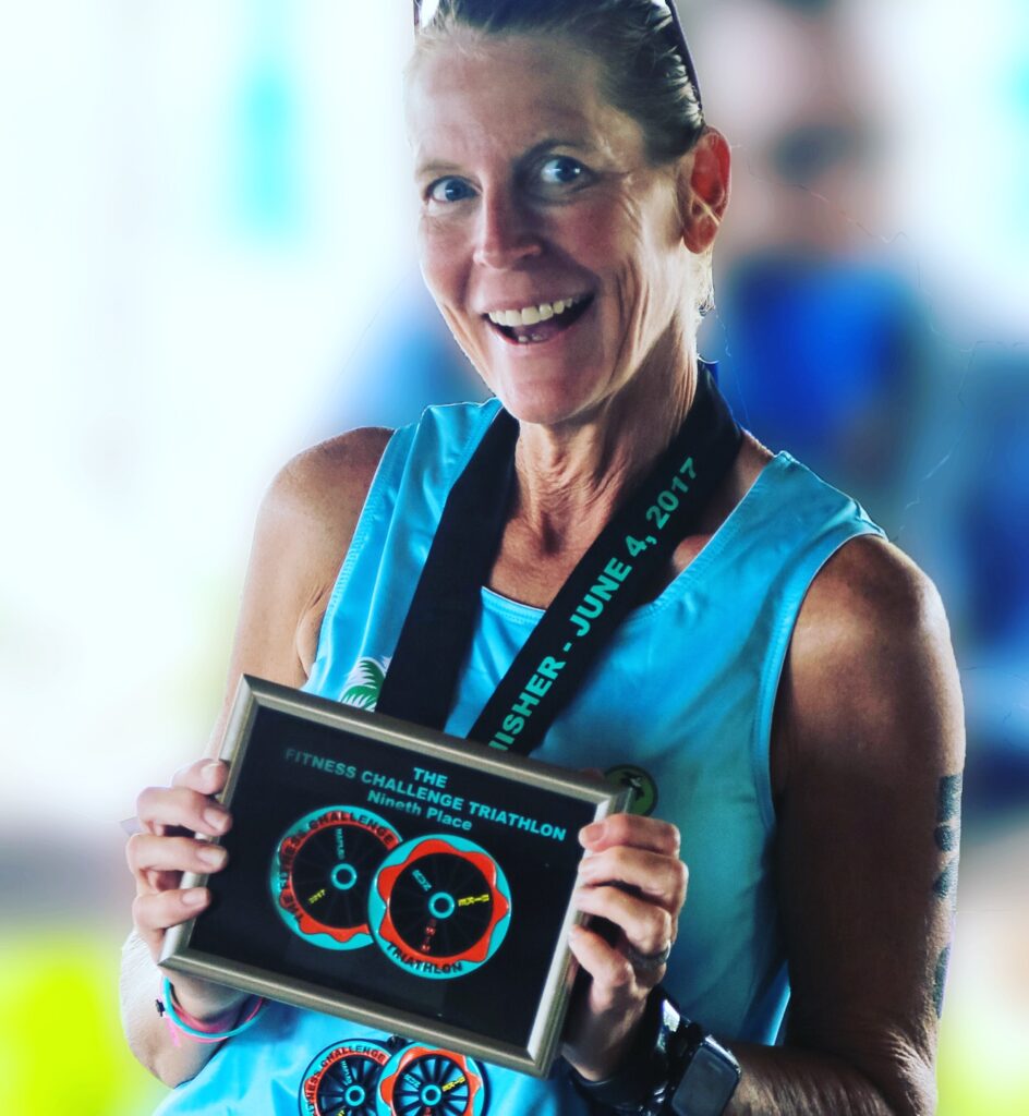 Triathlon coach Laurie Rose displaying here finishers plaque at a triathlon.